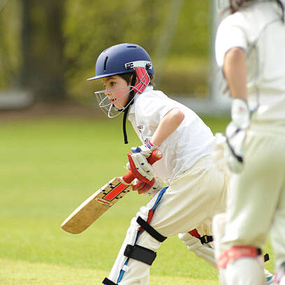 Young boy wearing protective clothing batting in a cricket match in England watched by the wicket keeper