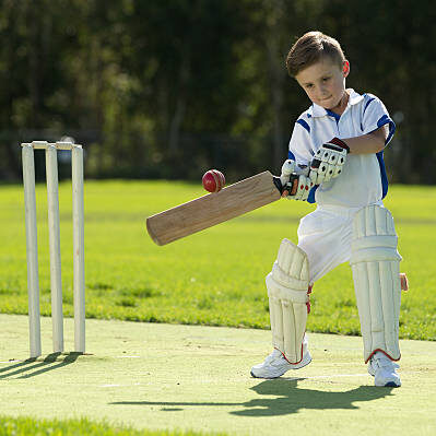 A small boy hits the ball while batting as he plays cricket